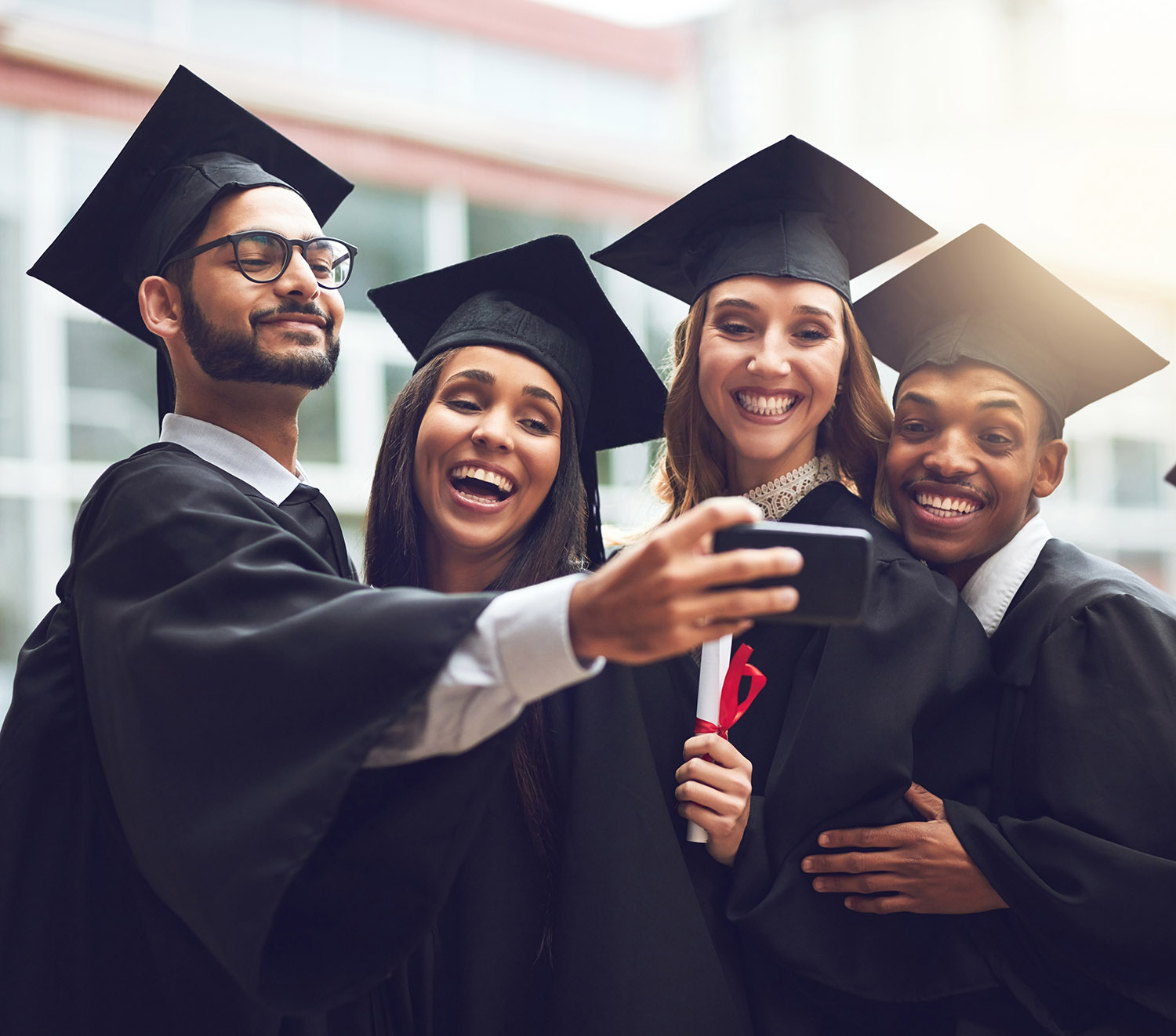 Four people standing in cap and gown taking a selfie. 